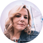 portrait of a woman with blonde curls and floral top, wearing a denim jacket in a softly lit background, woman with styled hair in circular frame