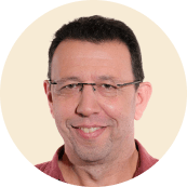 smiling man with glasses in a circular frame, casual portrait with neutral background and warm expression