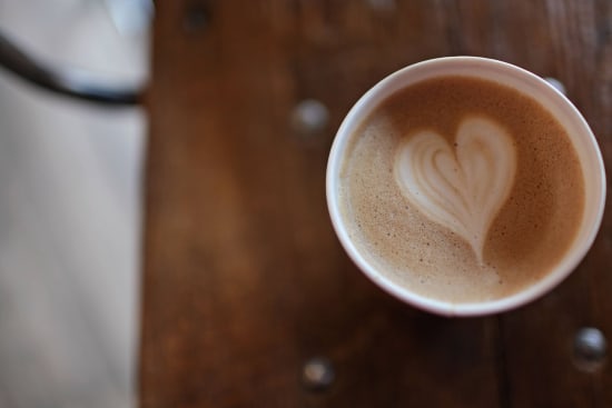 coffee cup with heart latte art on wooden table, warm coffee beverage in cozy atmosphere with creative design