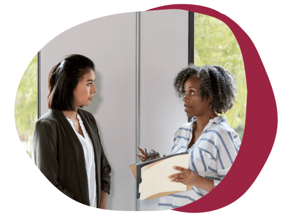 professional women discussing ideas in an office setting with a clipboard and natural light, diverse conversation with a clipboard