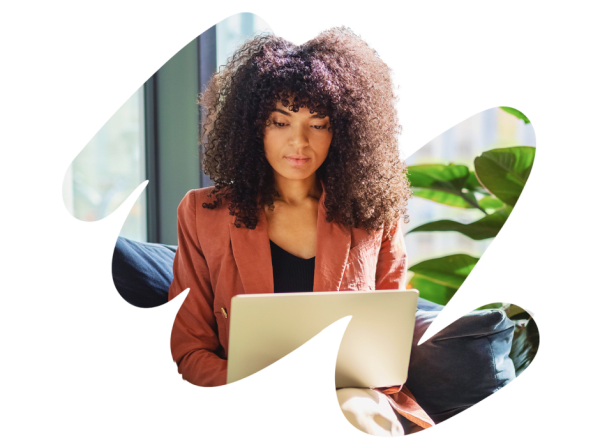 woman working on laptop at home with plants and natural light, curly hair professional in cozy workspace setting