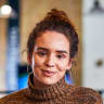 smiling woman in a cozy turtleneck sweater with hoop earrings, modern cafe background with warm lighting and textures