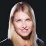 happy woman with long blonde hair and blue eyes, smiling on dark background, elegant attire with earrings and necklace