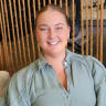 smiling woman in light green blouse sitting against a rope backdrop, warm atmosphere with cozy decor elements