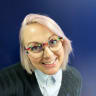 bright-eyed woman with pink hair and colorful glasses smiling against a blue background, female professional with playful style