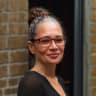 woman with glasses and bun hairstyle smiling against a brick wall, portrait of a confident woman in casual attire