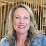 smiling woman with blonde, wavy hair and blue eyes wearing red lipstick, denim jacket with textured rope backdrop, cheerful portrait in modern setting, highlighting expressive features and vibrant style