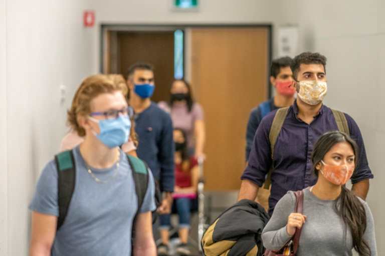 Colleges students filing into class while wearing protective face masks.