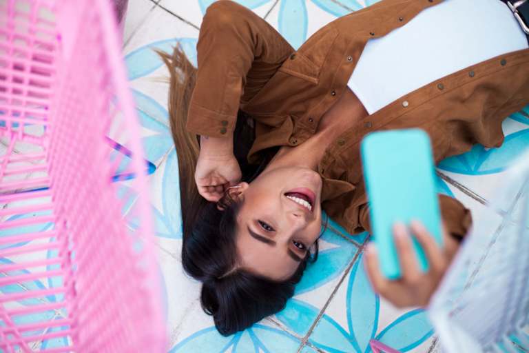 College student watches TikTok videos on her mobile phone while lying on her dorm room bed.
