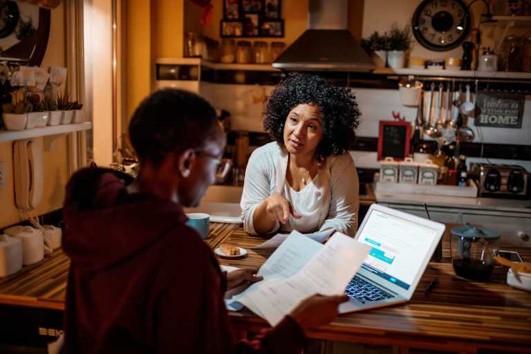 Mother and daughter sitting in the kitchen at home discussing college student loan payments.