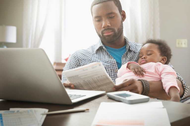 Father holding his baby daughter while trying to work from home.