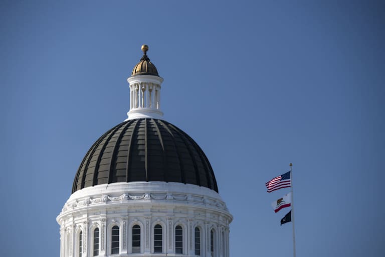 The American, California State, and POW/MIA flags fly next to the California State Capitol building in Sacramento, California