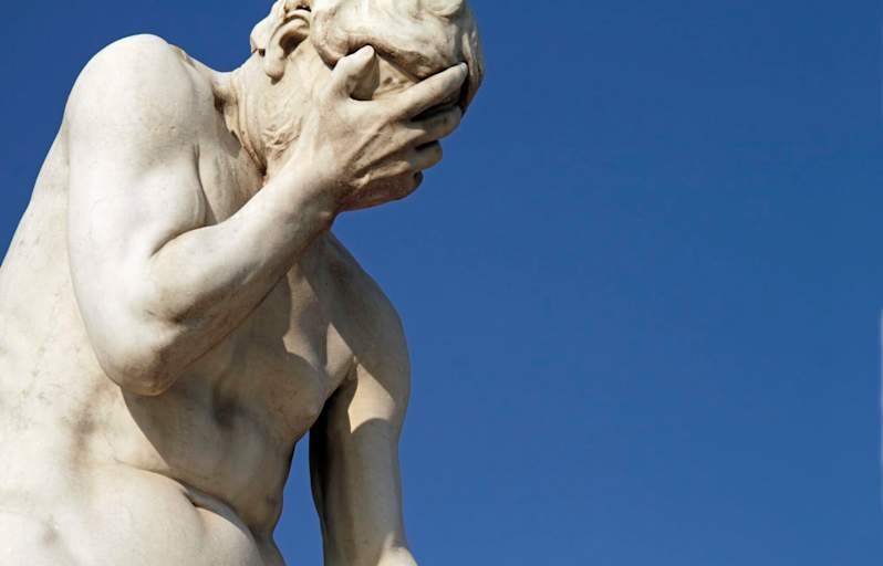 Photo of a marble statue showing a person Facepalming, Head In Hands against a clear blue sky background