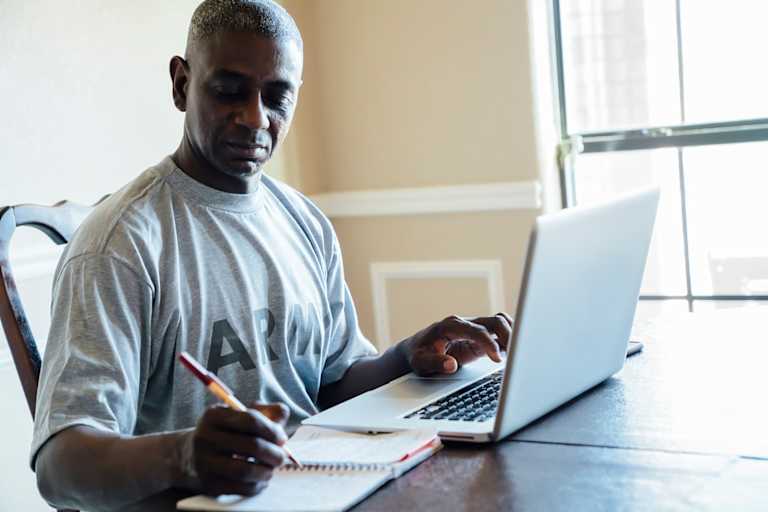 Veteran using laptop and notebook at table