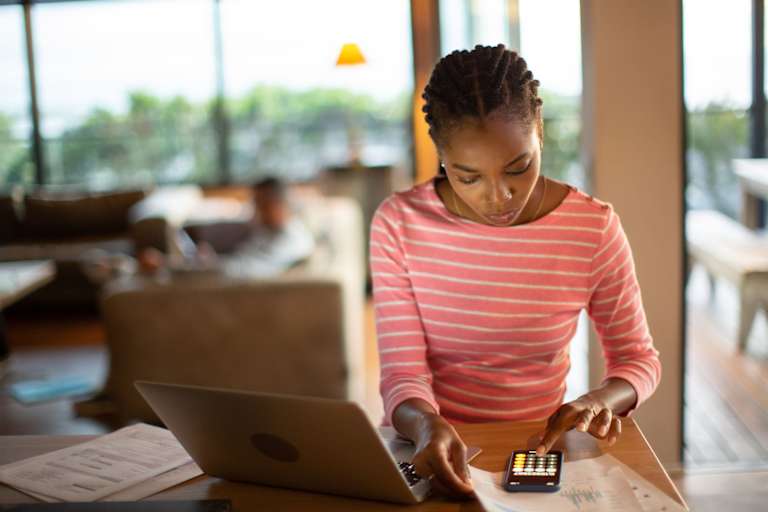 Person at home using calculator on phone while on laptop