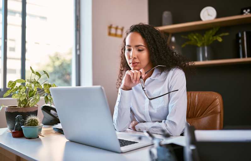 Female accountant sitting at a desk in her office. She has taken her glasses off, and is reading documents on her laptop computer.
