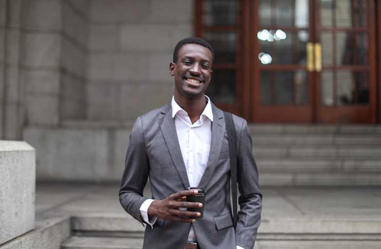 Black male lawyer standing outside a courthouse. He is wearing a gray business suit. He is facing the camera and smiling.