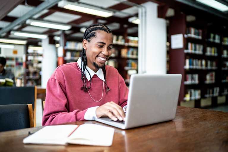 Black male college student studying on his laptop in a library on campus.