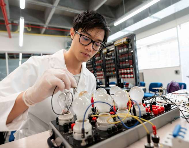 An Asian male college student testing electronics in a laboratory on campus.