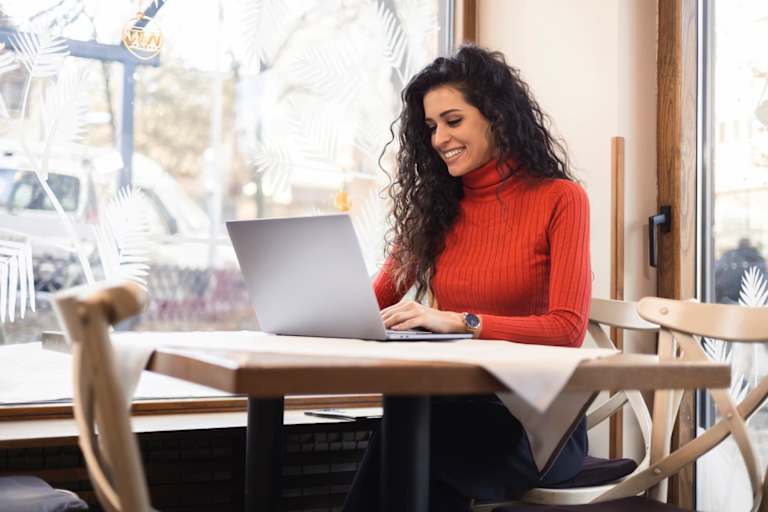 Female college student sitting inside a cafe. She is typing a class assignment on her laptop.