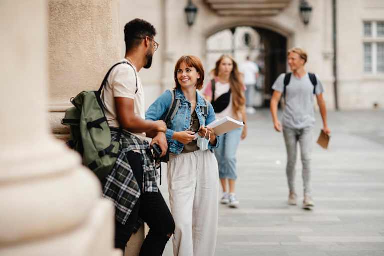A Black male and a Caucasian female student chat outside on their college's campus before class begins.