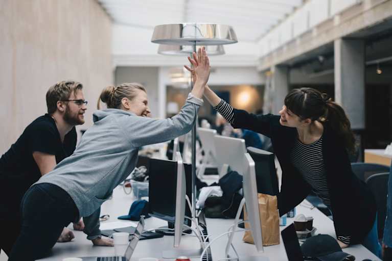 Happy female computer programmers giving high-five over desk in office