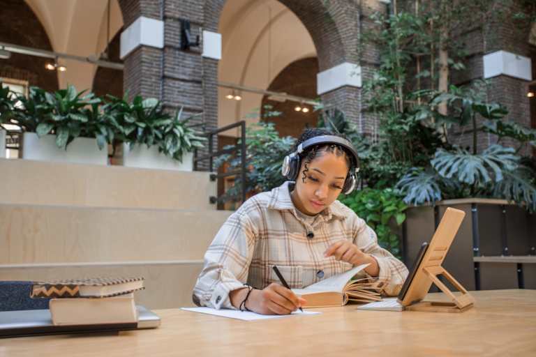 Black female college student studying in a public library. She is sitting at a table taking notes for an upcoming class paper.