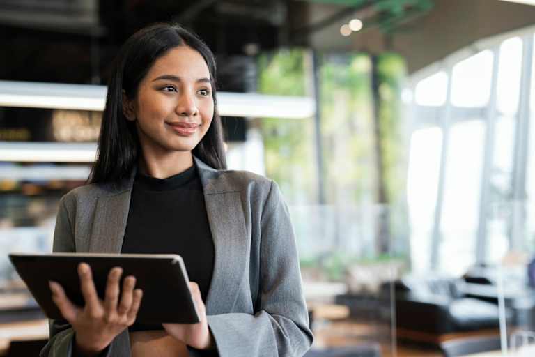Female accountant using a tablet device while standing and looking at a coworker off screen in a financial office.