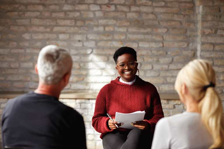 Black female therapist speaking to a mid-age couple during a counseling session in her office.