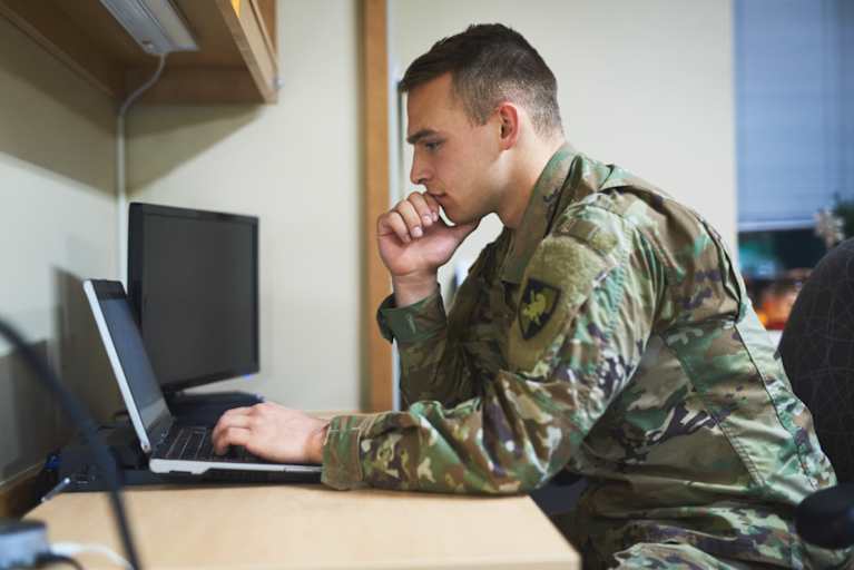 ROTC military college student studying on his laptop in a dorm room on campus.
