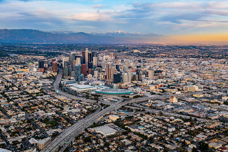 Aerial view of downtown Los Angeles, with the Sierra Mountain range in the background, at sunset.