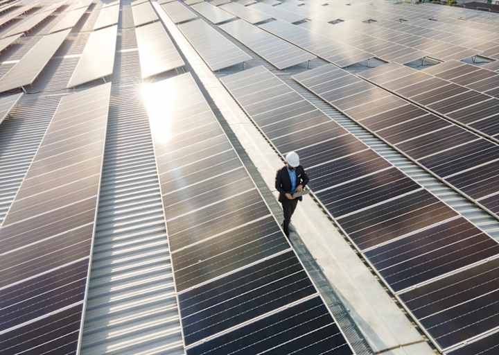 Caucasian male solar power plant engineer examining photovoltaic panels at a solar farm.