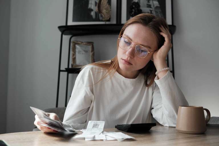 Stressed female college student sitting at her kitchen table at home. She is looking through receipts while trying to budget her monthly bills.