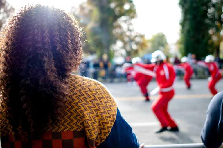 Black female college student watching her HBCU's homecoming parade outdoors.