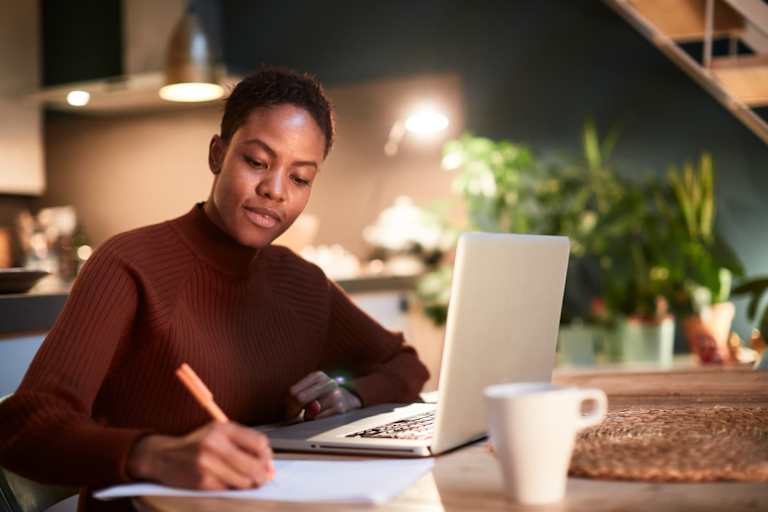 Black female student budgeting college expenses on her laptop at home.