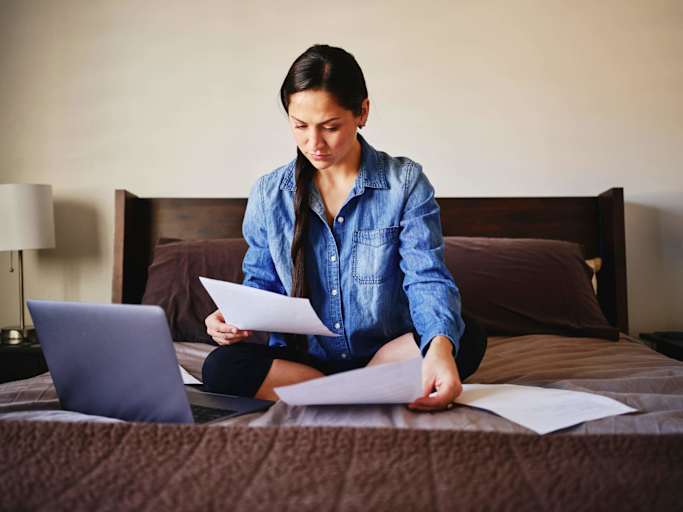 A woman sitting on her bed in a home looking through finances.