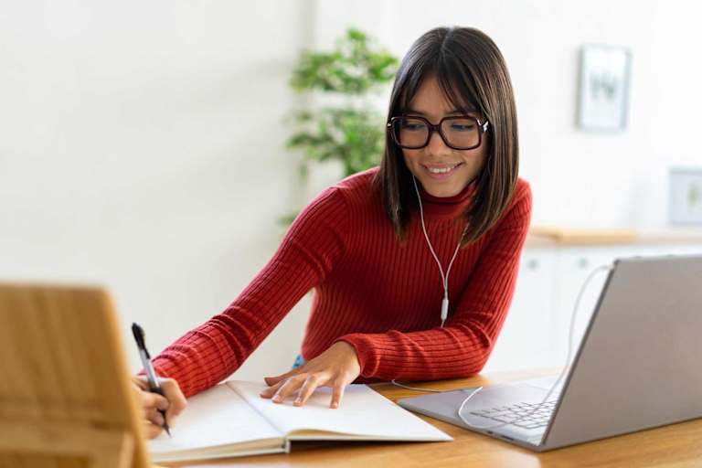 Smiling young woman writing in notebook on desk at home