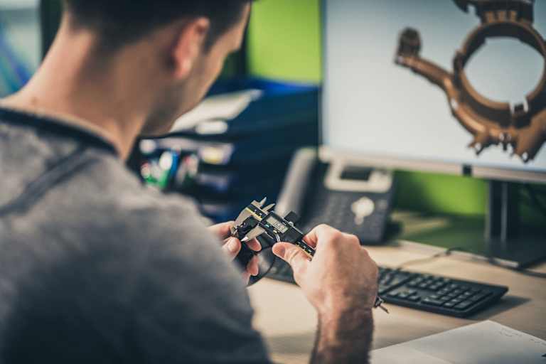 Engineer measuring a machine part while working on a 3D model