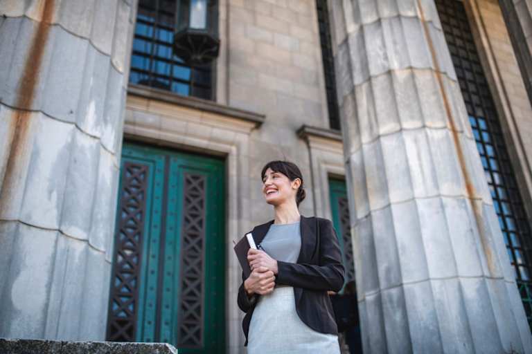 Woman in professional clothing holding a book standing in front of historical building