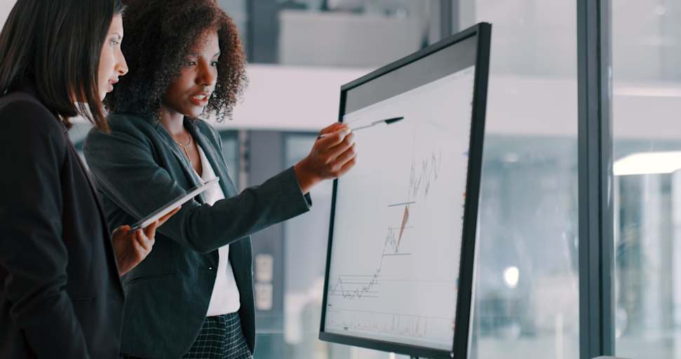 Shot of two young businesswomen using an interactive whiteboard to analyze data in a modern office