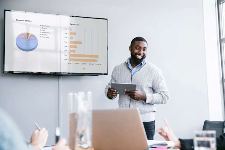 Smiling businessman holding tablet computer explaining graphs in meeting at board room