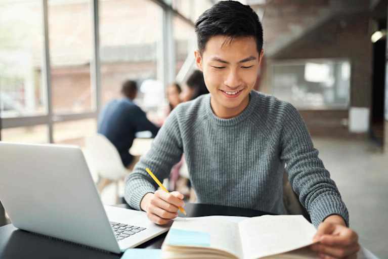 Criminal justice student studying with laptop and book open, smiling.
