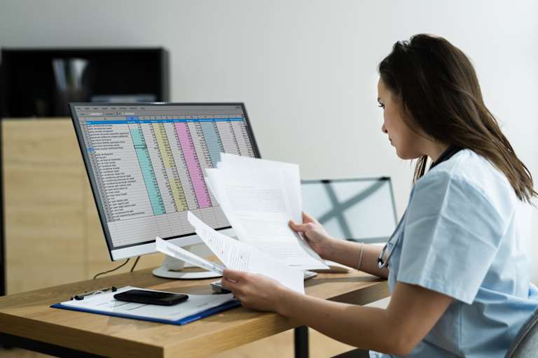 RN Coder looking at paperwork at computer desk