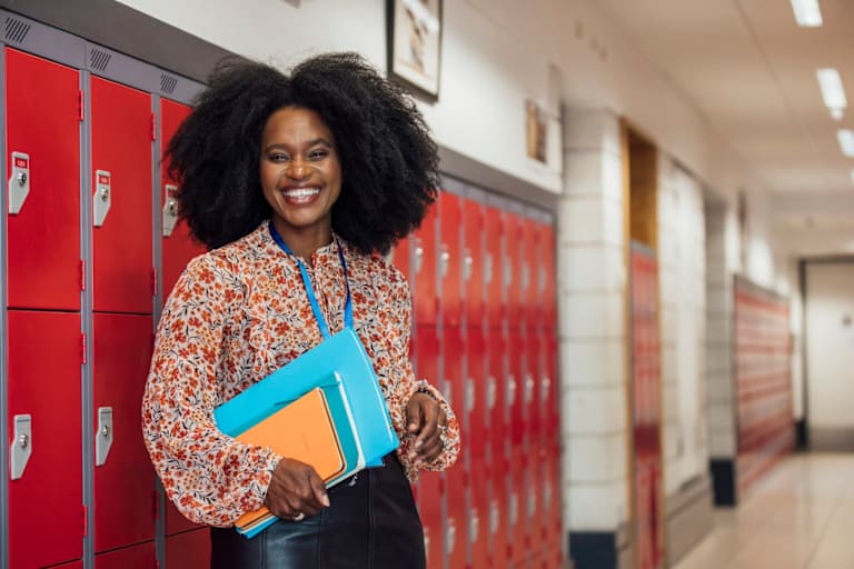 A high school principal stands in the hallway with documents.