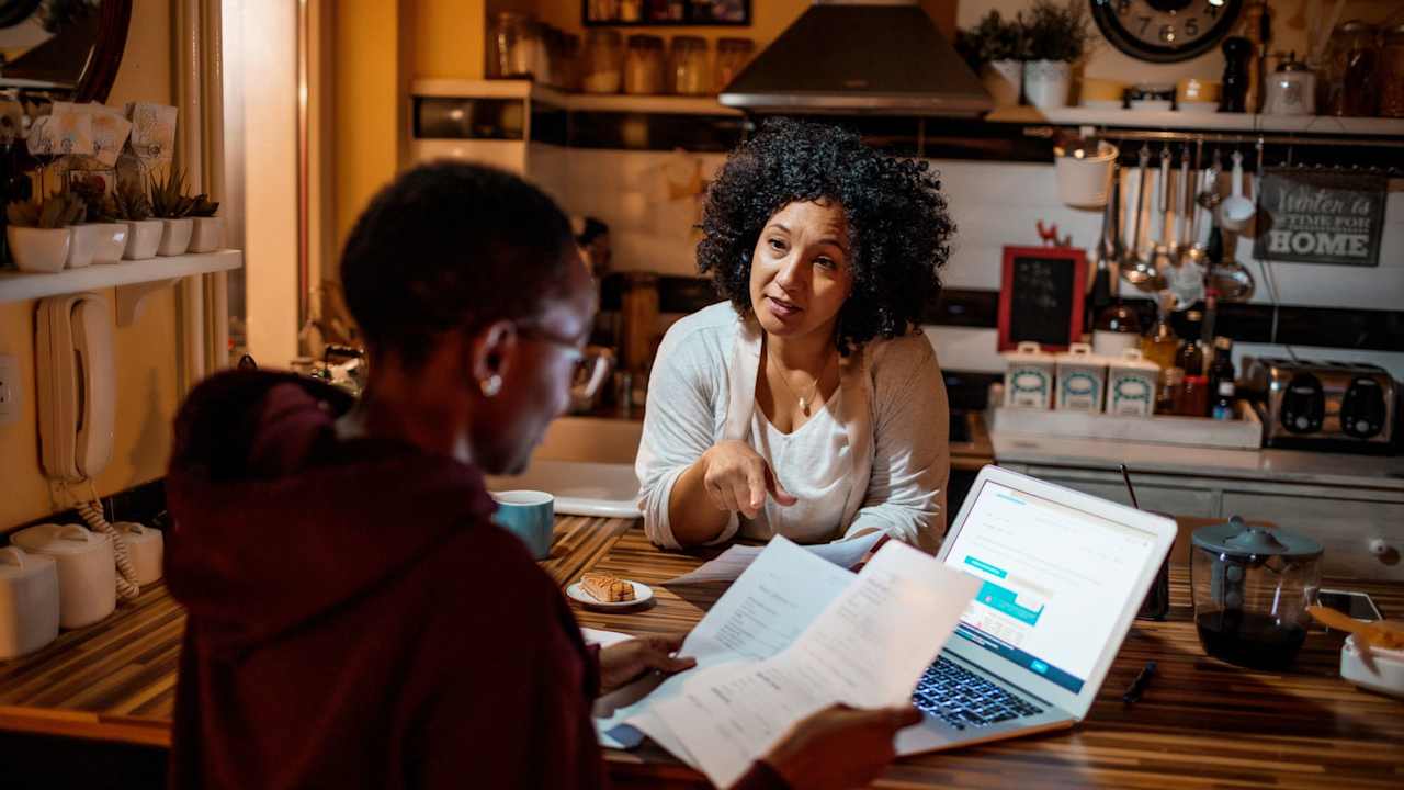 Mother and daughter sitting in the kitchen at home discussing college student loan payments.