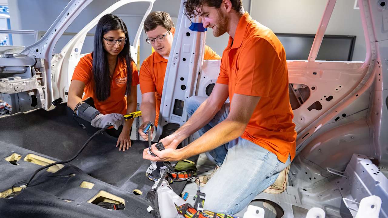 Clemson Launches Nations First Bachelor of Science in Automotive Engineering. Students wearing orange polo shirts working on the interior of a car.