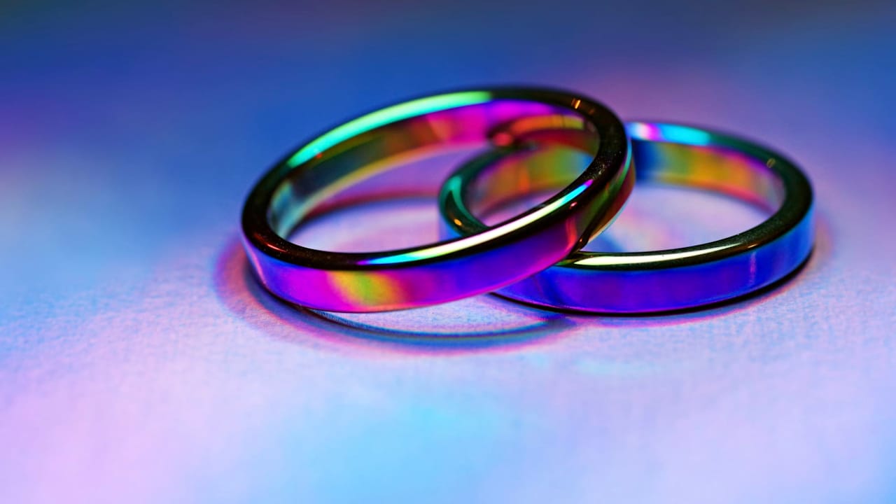Two rainbow titanium-coated band rings on holographic foil paper with vibrant light effects