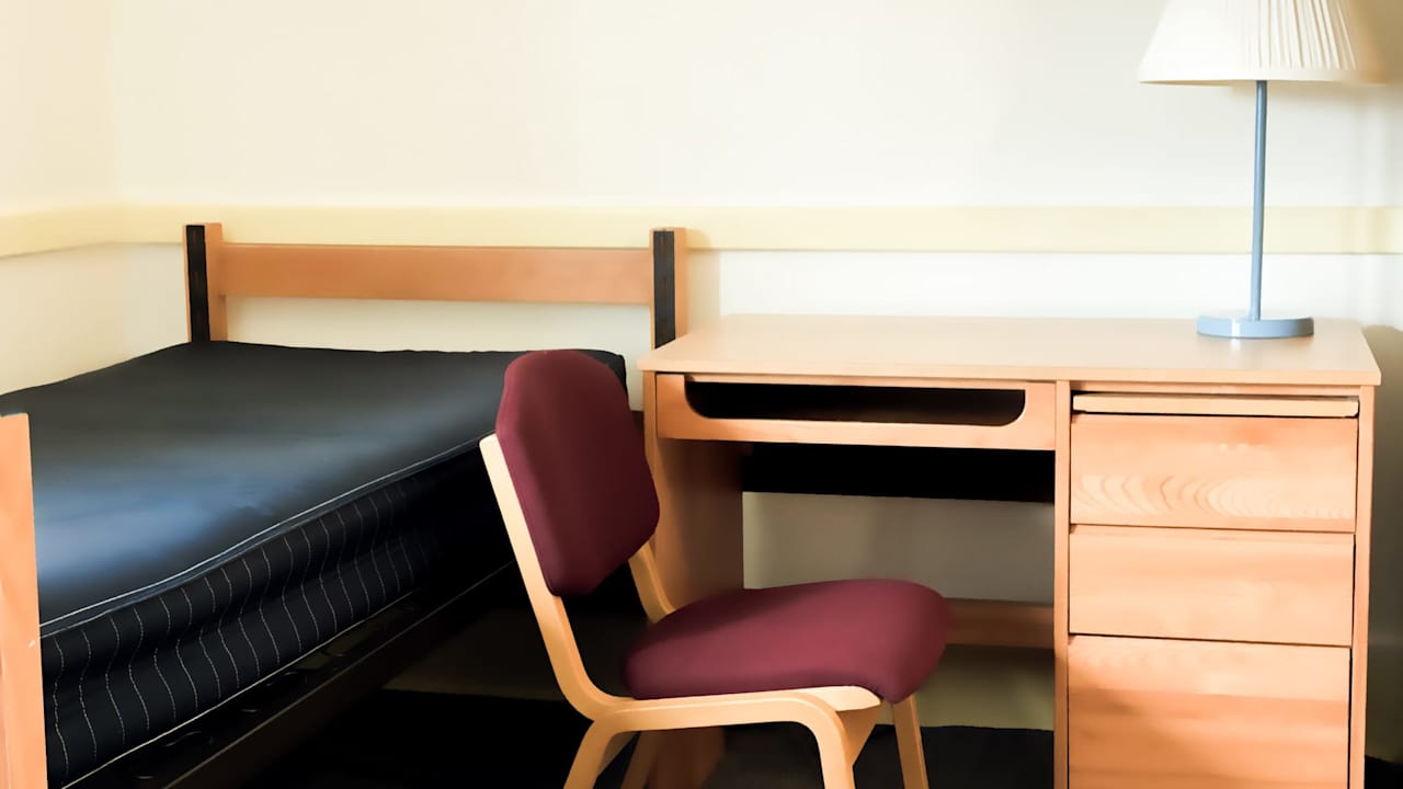 Empty student dormitory room with bed, desk, lamp, chair