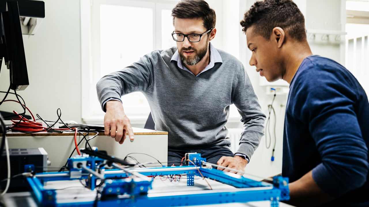 An engineering tutor assisting one of his students with a technical problem during teaching session at university.