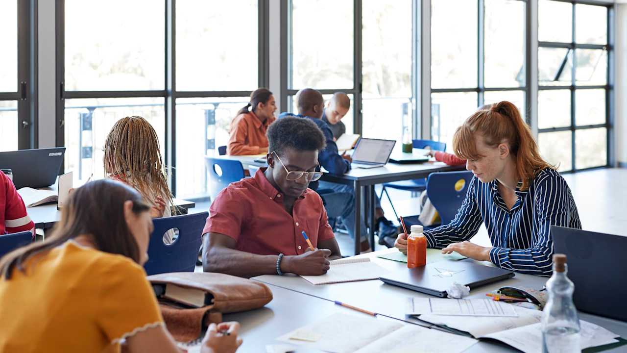 Young female and male university students studying while sitting on desk in classroom